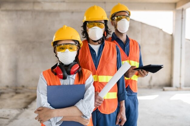 colleagues-with-safety-equipment-working-with-blueprints_23-2148908431